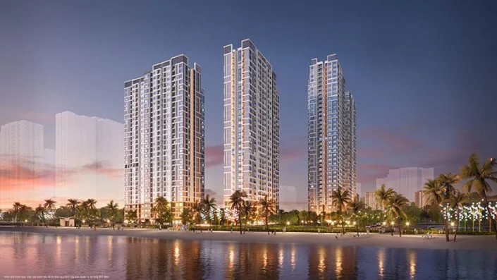 Ba tòa căn hộ cao tầng được chiếu sáng rực rỡ nhìn từ mặt nước vào buổi tối, hàng cọ ven bờ