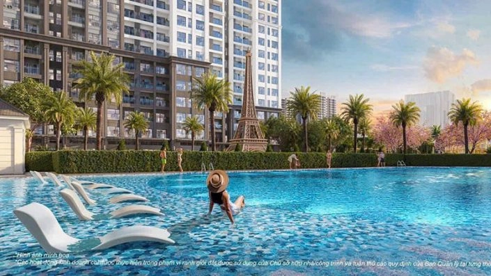 Bể bơi ngoài trời với ghế thư giãn, người bơi lội và tháp Eiffel thu nhỏ phía sau