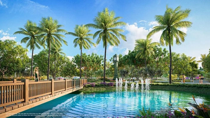 Cầu gỗ bắc qua hồ nước có đài phun nước, xung quanh là hàng cọ và cây xanh trong khuôn viên dự án